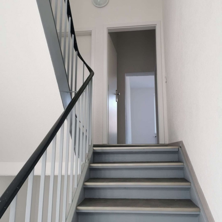 Helle Treppe mit Metallgeländer und Türen im Innenbereich.