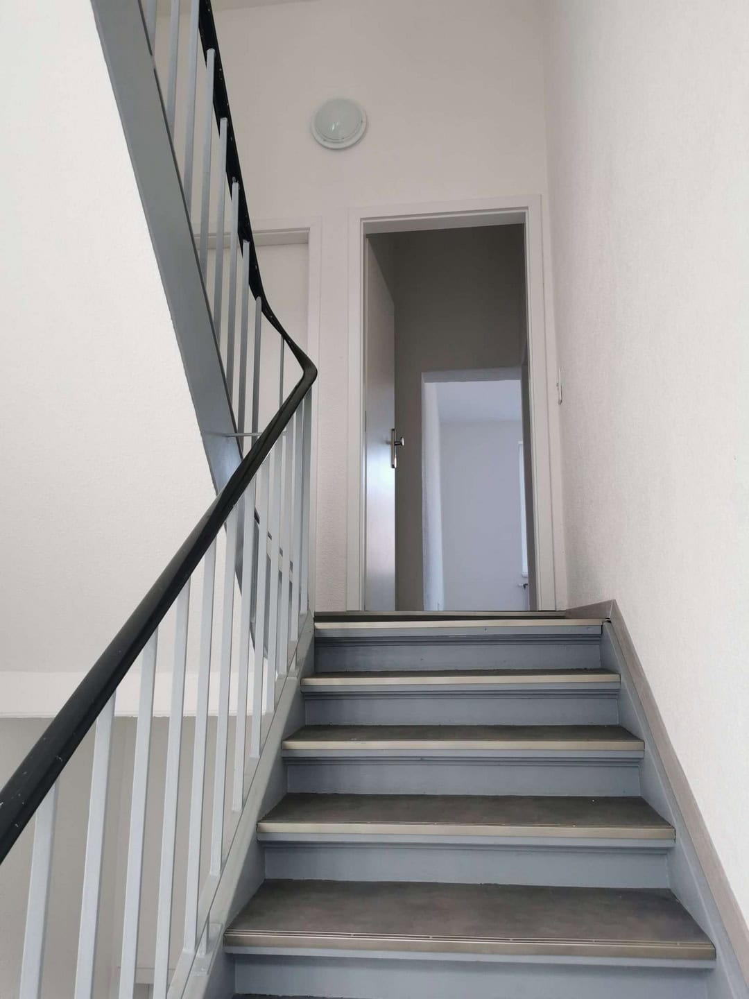 Helle Treppe mit Metallgeländer und Türen im Innenbereich.