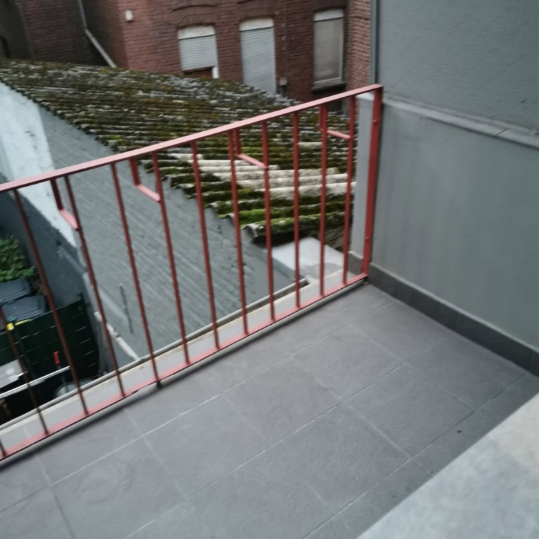 Rote Balkonbrüstung vor veraltem Dach mit Mauer, Blick auf Altbauten, urbanes Wohnen, Balkon, Renovierung, Dächer, Energieeffizienz, Stadtleben.