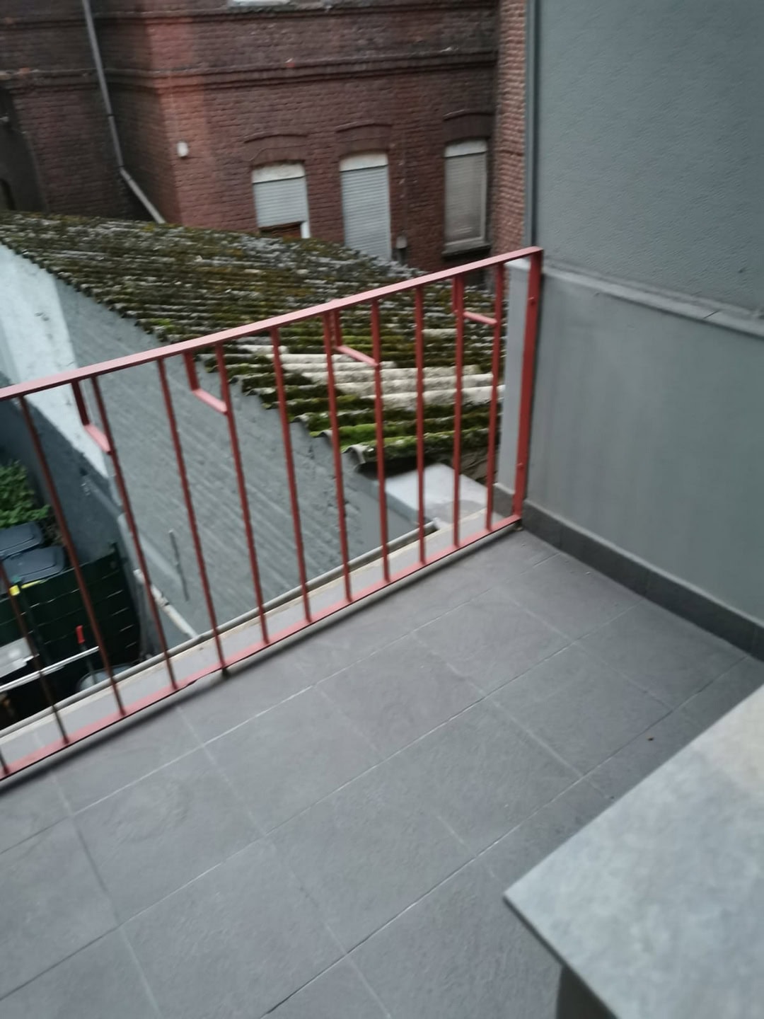 Rote Balkonbrüstung vor veraltem Dach mit Mauer, Blick auf Altbauten, urbanes Wohnen, Balkon, Renovierung, Dächer, Energieeffizienz, Stadtleben.