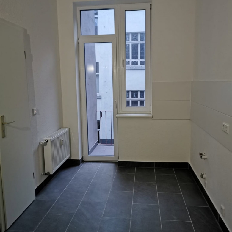 Helle, moderne Küche mit dunklen Fliesen, weißem Fenster und Zugang zum Balkon, funktional gestaltet, ideal für Renovierungen und Neubauten.