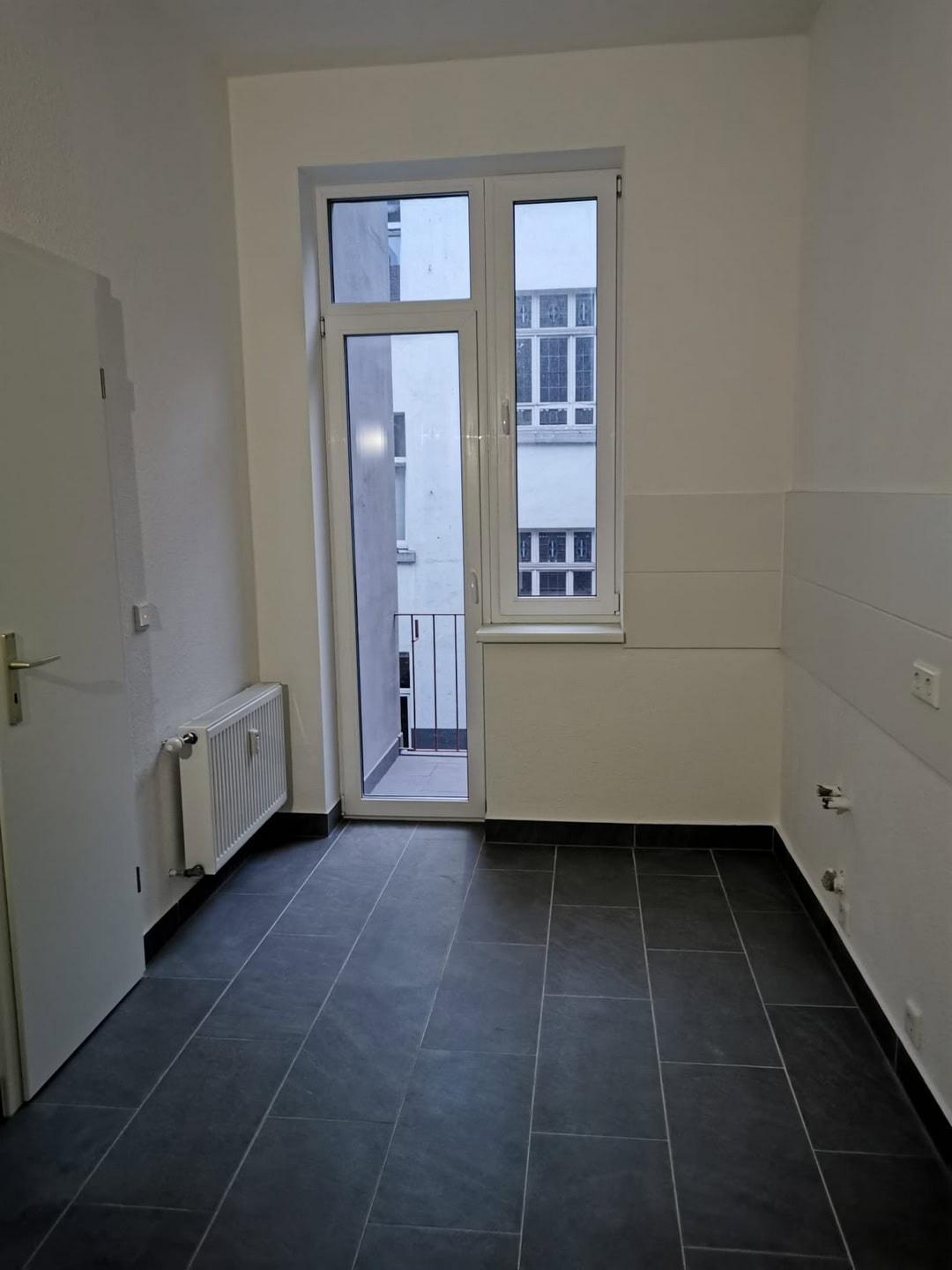 Helle, moderne Küche mit dunklen Fliesen, weißem Fenster und Zugang zum Balkon, funktional gestaltet, ideal für Renovierungen und Neubauten.