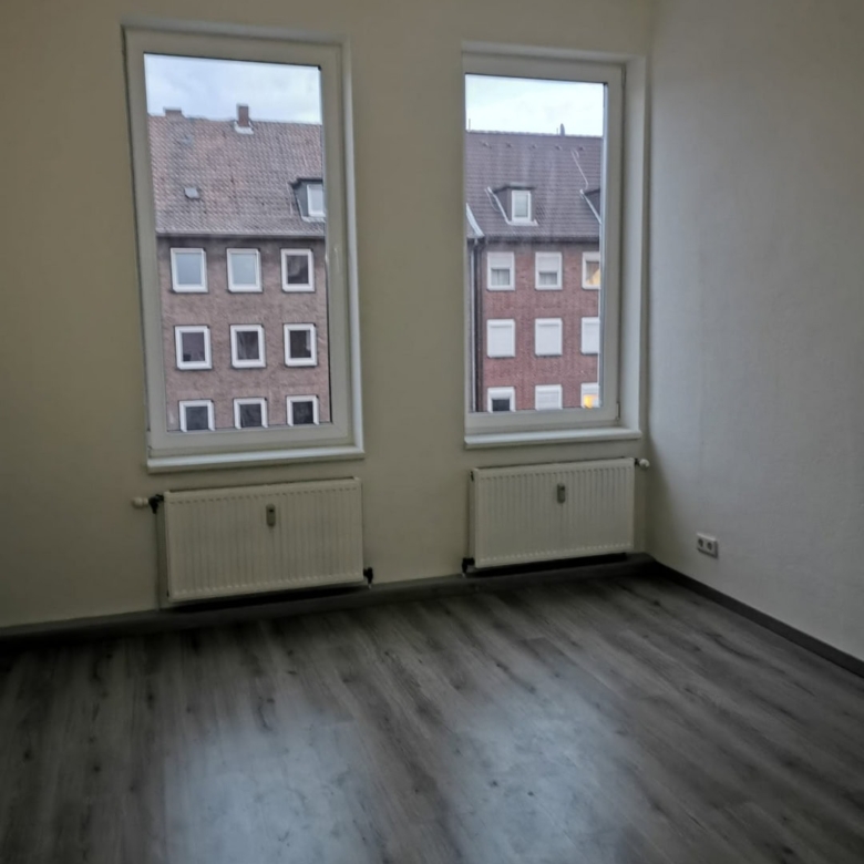 Moderne Wohnung mit großen Fenstern und Blick auf Nachbargebäude, Parkettboden, helle Wände, ideal für Eigenheim oder Vermietung, hochwertige Bauausführung.