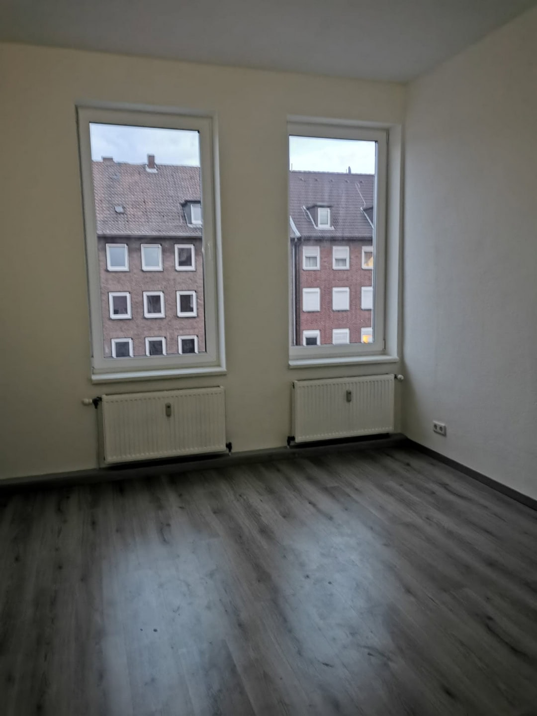 Moderne Wohnung mit großen Fenstern und Blick auf Nachbargebäude, Parkettboden, helle Wände, ideal für Eigenheim oder Vermietung, hochwertige Bauausführung.