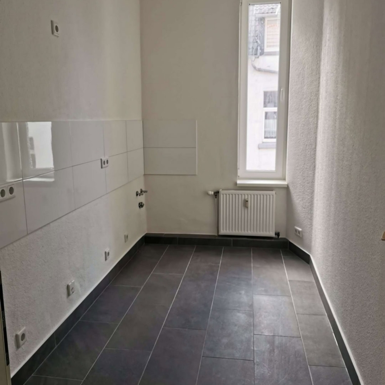 Helle, moderne Küche mit weißen Wänden, großen Fliesen und einem großen Fenster für natürliches Licht.