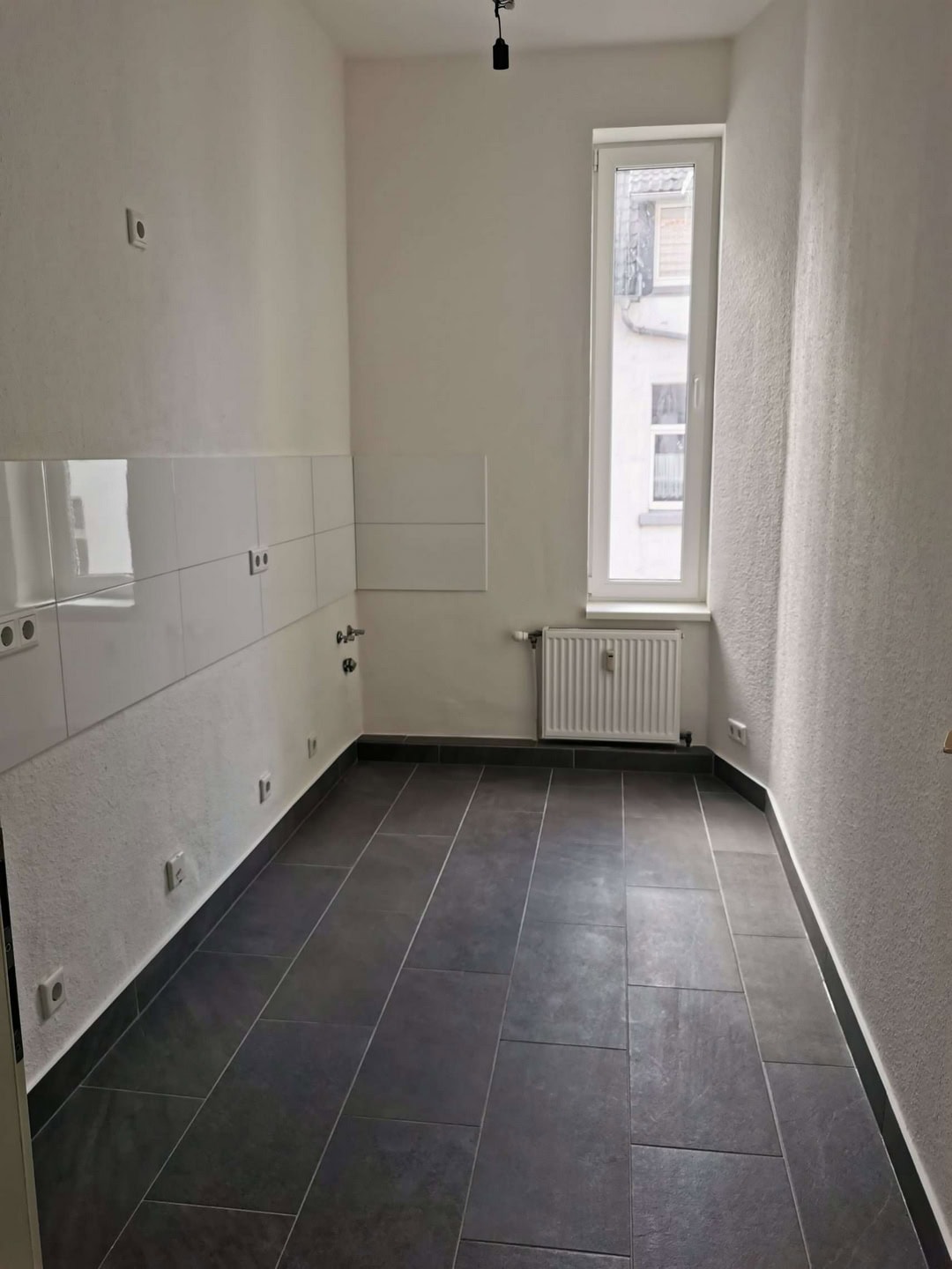 Helle, moderne Küche mit weißen Wänden, großen Fliesen und einem großen Fenster für natürliches Licht.