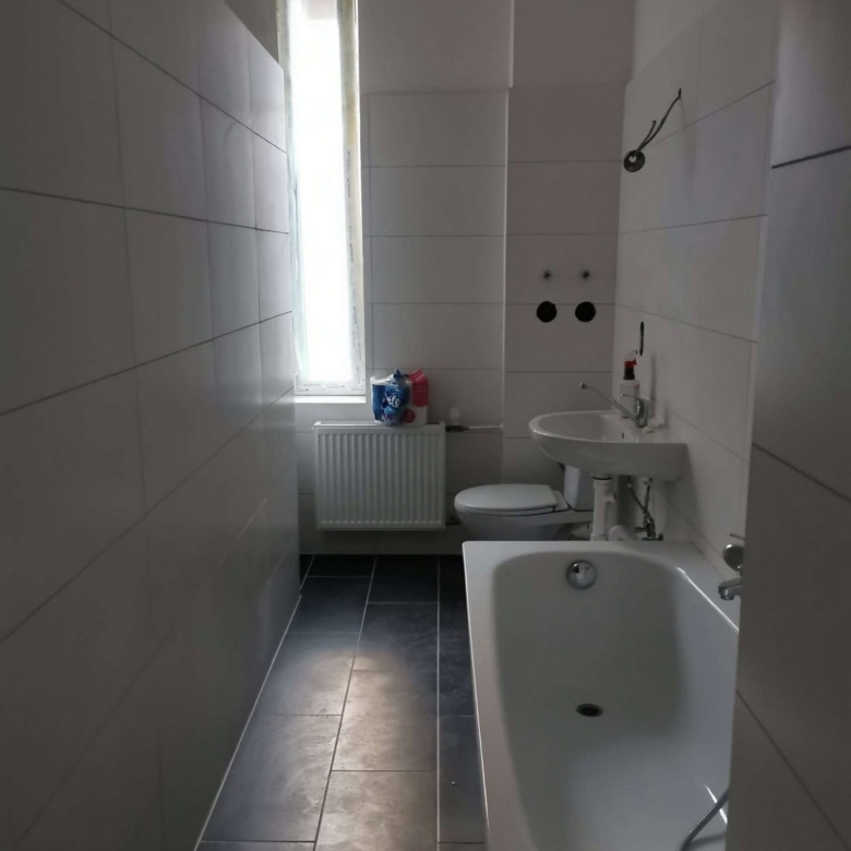 Moderne Badezimmergestaltung mit weißen Wandfliesen und dunklem Bodenbelag, inklusive Badewanne, Waschbecken und WC - hochwertige Sanitärinstallation vom Profi.