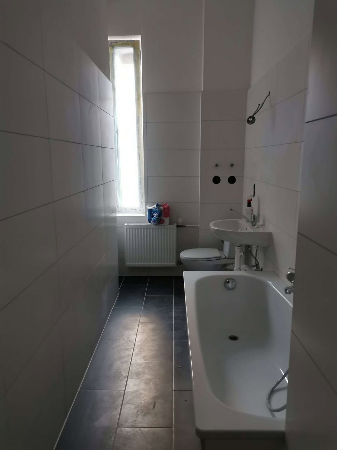 Moderne Badezimmergestaltung mit weißen Wandfliesen und dunklem Bodenbelag, inklusive Badewanne, Waschbecken und WC - hochwertige Sanitärinstallation vom Profi.