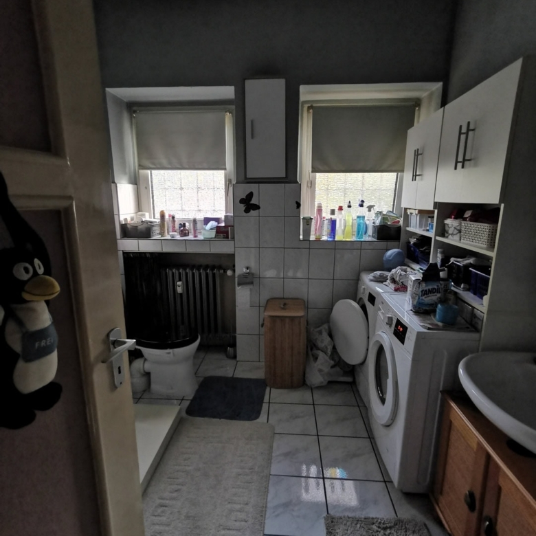 Просторная ванная комната с стиральной машиной, раковиной и окнами с шторками, много хранения и уборочной продукции, уютное пространство для домашнего комфорта.