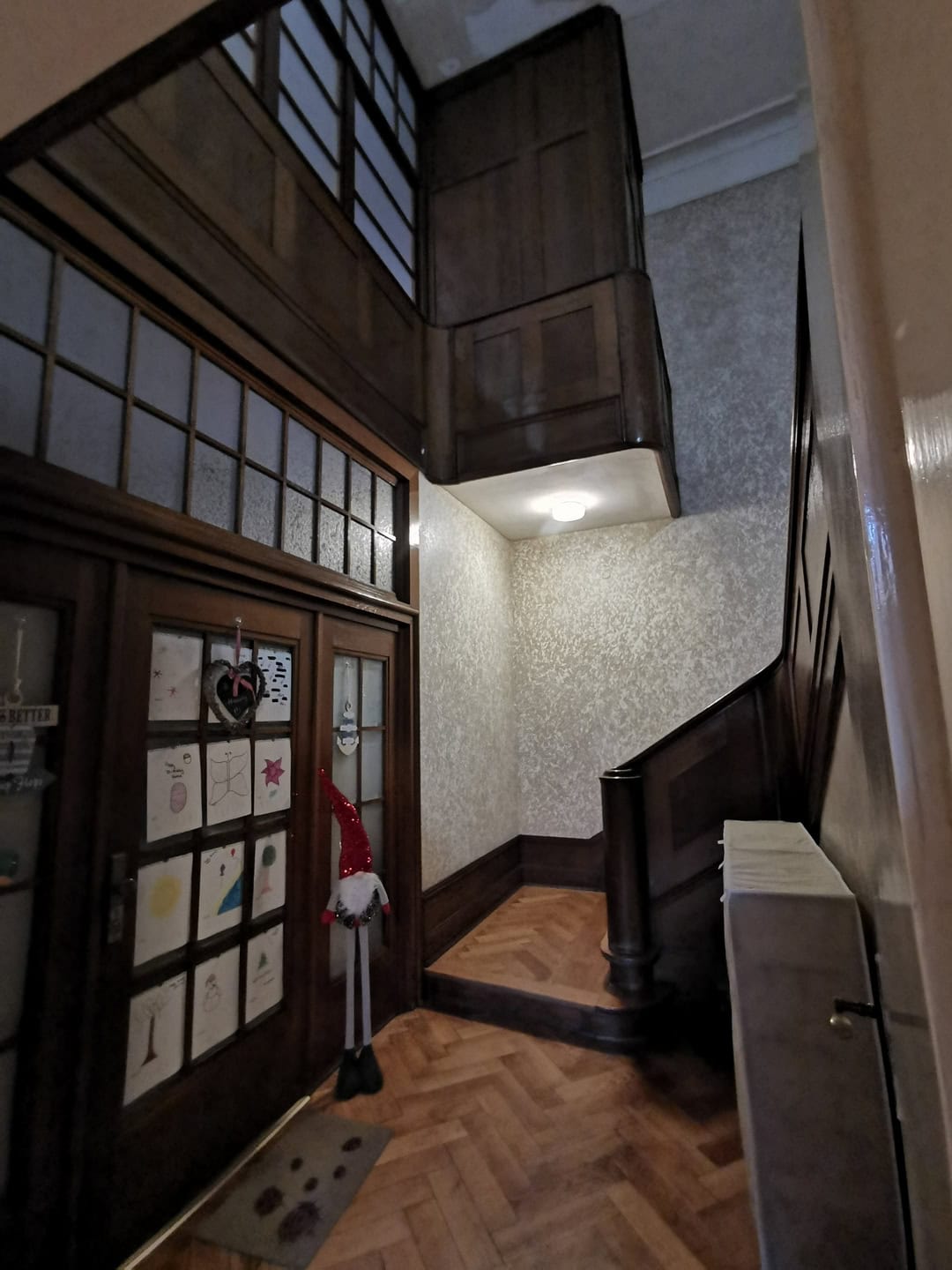 Угловая лестница из тёмного дерева в прихожей с декоративными стенами и паркетным полом, уютное интерьерное решение.