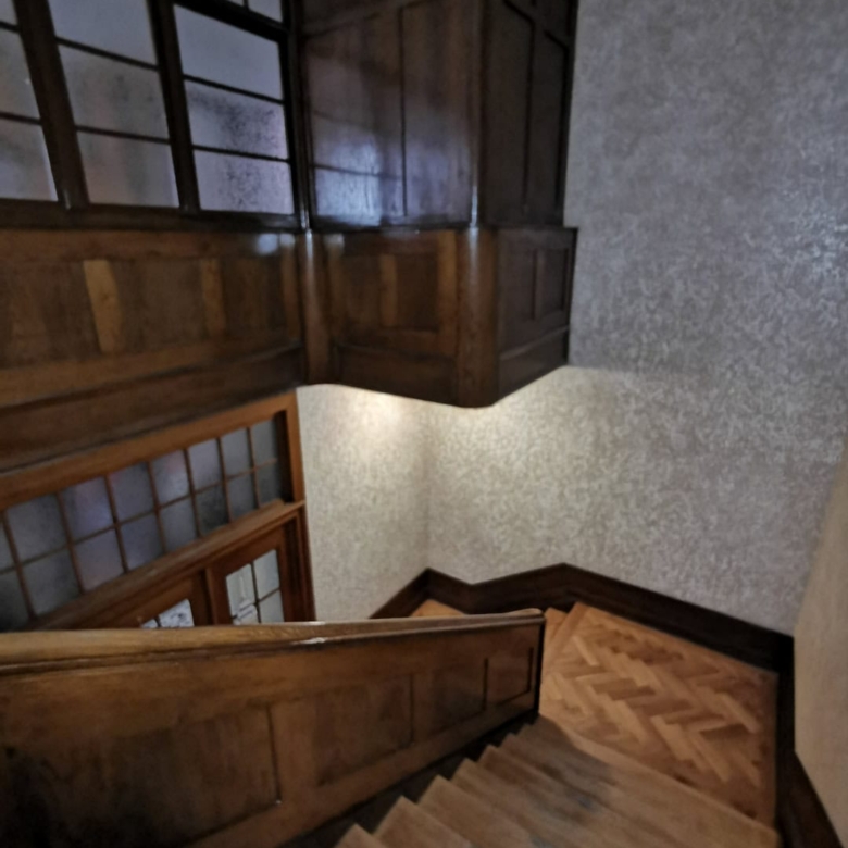 Мягкая деревянная лестница в доме с деревянными перилами и панелями, внутренняя отделка с теплым освещением, уютное интерьерное пространство, дизайн в классическом стиле, ремонт и строительство, отделочные работы, деревянные элементы.