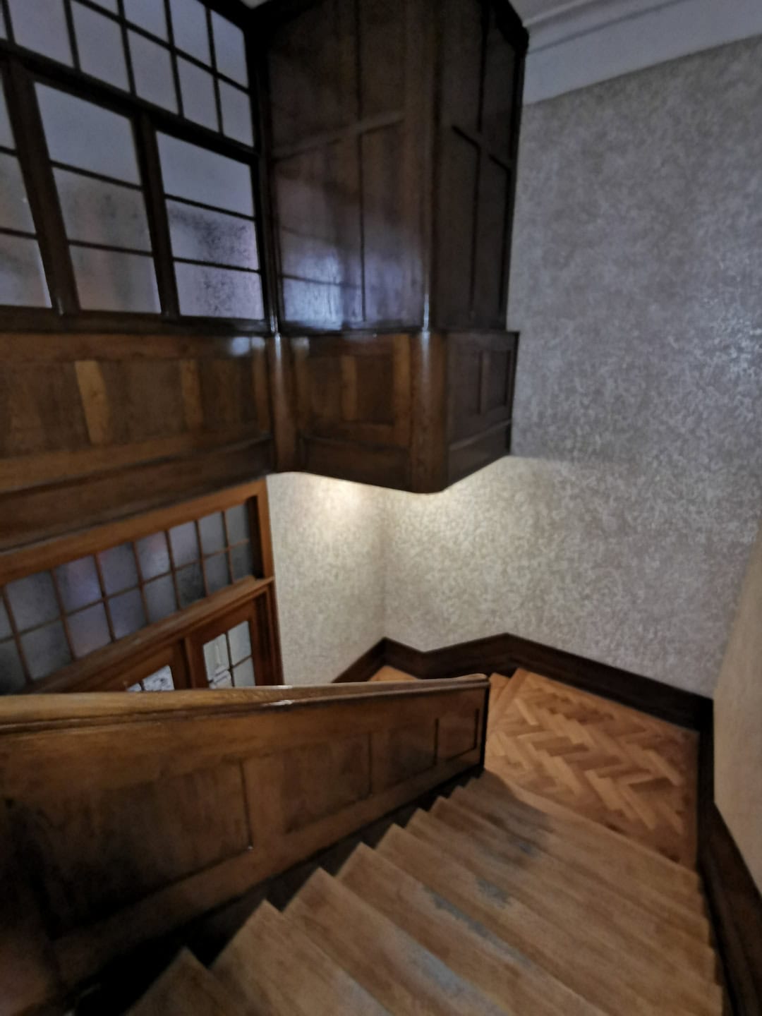 Мягкая деревянная лестница в доме с деревянными перилами и панелями, внутренняя отделка с теплым освещением, уютное интерьерное пространство, дизайн в классическом стиле, ремонт и строительство, отделочные работы, деревянные элементы.