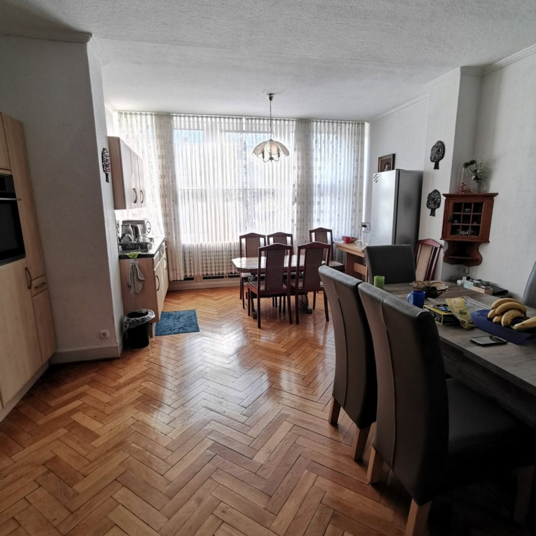 Уютная гостиная и кухня со светлыми жалюзи, деревянным паркетом и кухонной мебелью, идеально подходящая для семейных обедов и отдыха, демонстрирующая стильный дизайн интерьера.