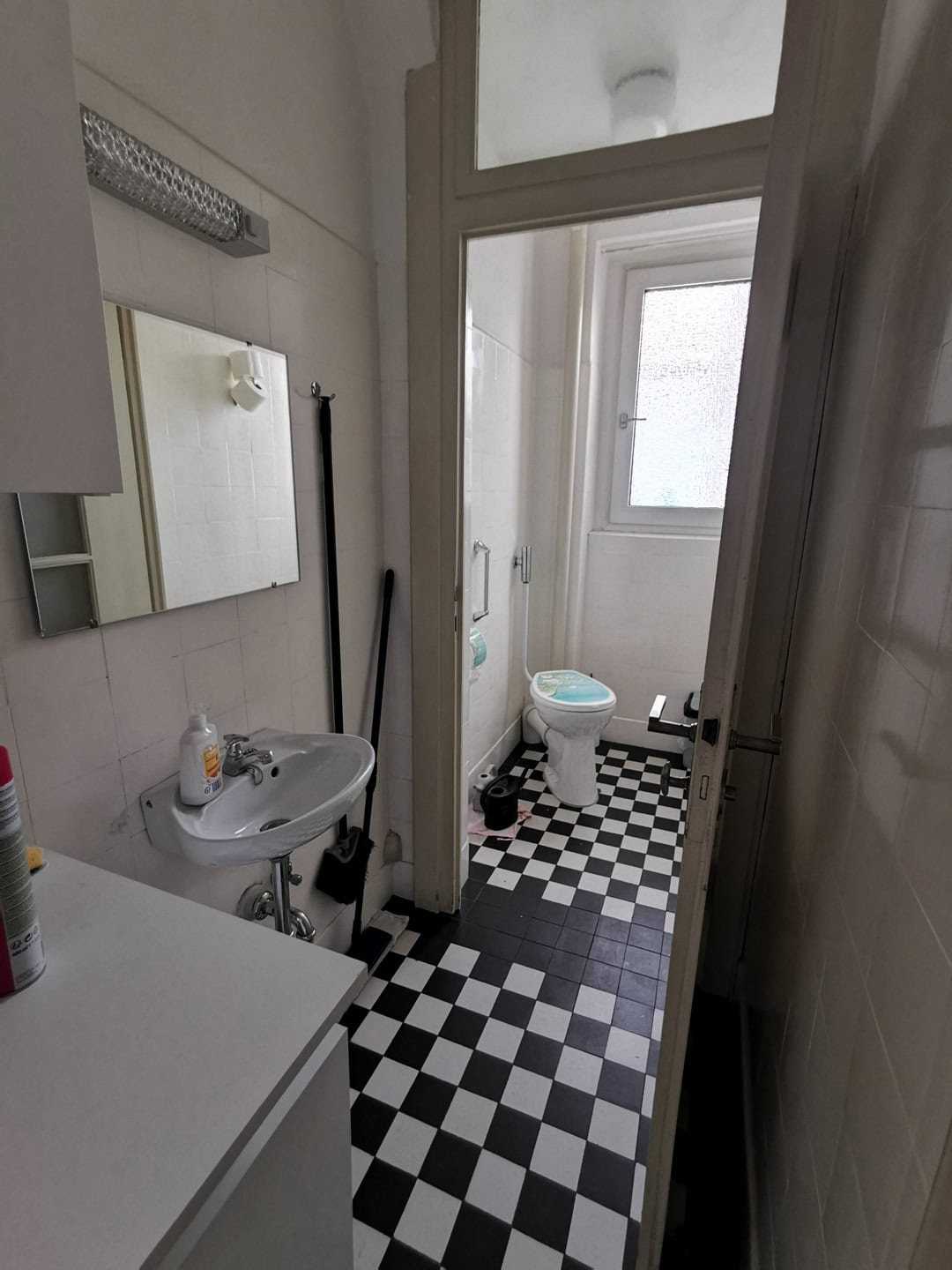 Маленькая ванная комната с туалетом и раковиной, светлый интерьер, окна для дополнительного естественного освещения, практическое решение для компактных пространств.