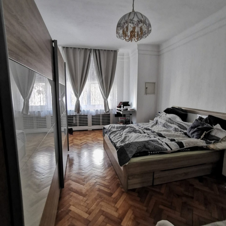 Уютная спальня с крупной кроватью, деревянным паркетом и светлыми шторами на окне, свет и комфорт в интерьере.