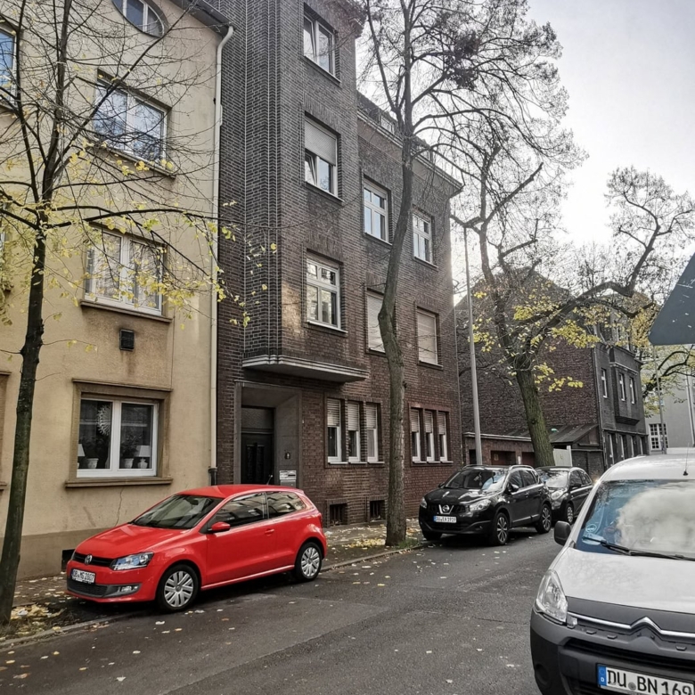 Современное жилое здание на улице с паркингом, архитектура в стиле современности, фасад с кирпичной отделкой, жилые автомобили на фоне деревьев.