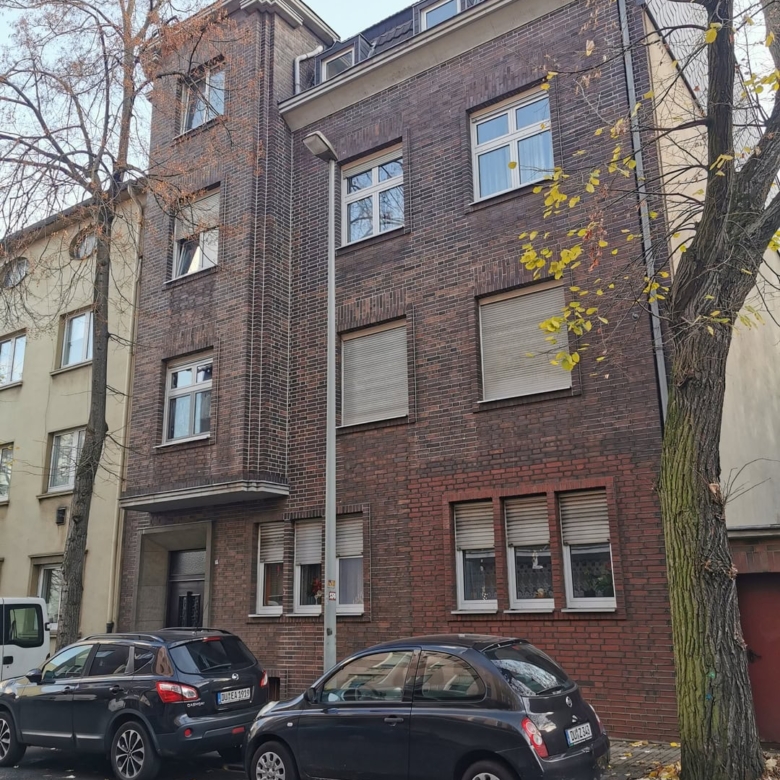 Кирпичный жилой дом с фасадом из коричневого кирпича, современными окнами и парковкой на переднем плане, окруженный деревьями, осень.