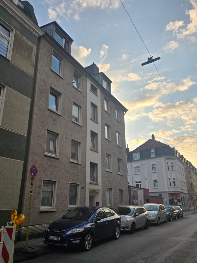 Alt: Mehrfamilienhaus in urbaner Umgebung mit Parkplätzen und alten Gebäuden, typisch für Berlin, Deutschland.