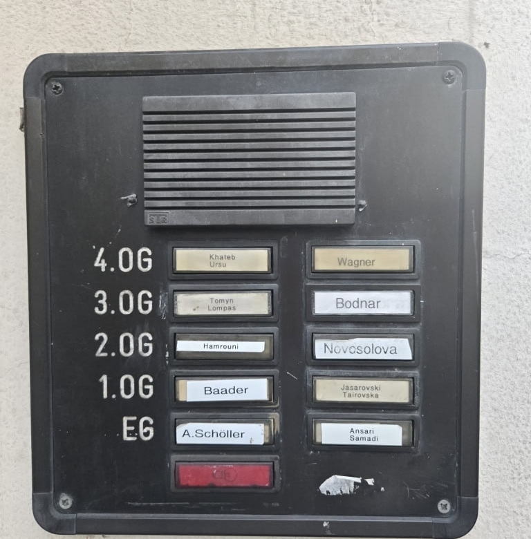 Alt: Hausnummern- und Namensschild mit verschiedenen Namen für Apartments oder Wohnungen, Außenansicht.