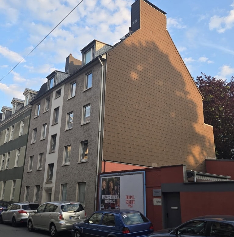 Attraktives Mehrfamilienhaus in urbaner Lage mit modernem Fassadenstil und Parkplatz vor dem Gebäude.
