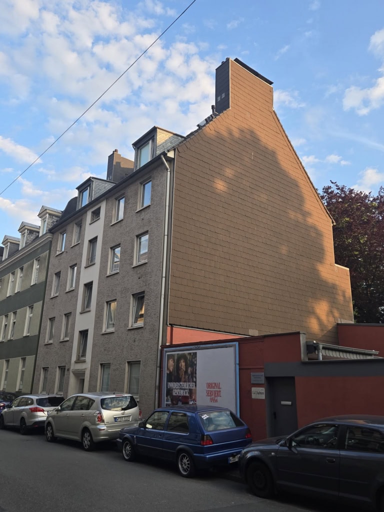 Attraktives Mehrfamilienhaus in urbaner Lage mit modernem Fassadenstil und Parkplatz vor dem Gebäude.