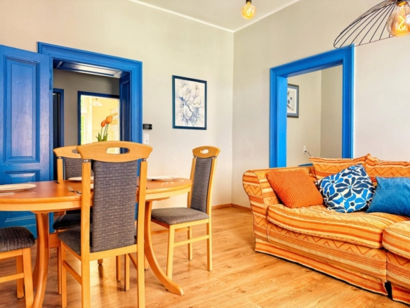 Gemütliches Wohnzimmer mit blauer Türrahmen, bequemem Sofa mit bunten Kissen und modernem Essbereich, Dekor im skandinavischen Stil, ideal für Ferienwohnungen, DEM Gruppe.