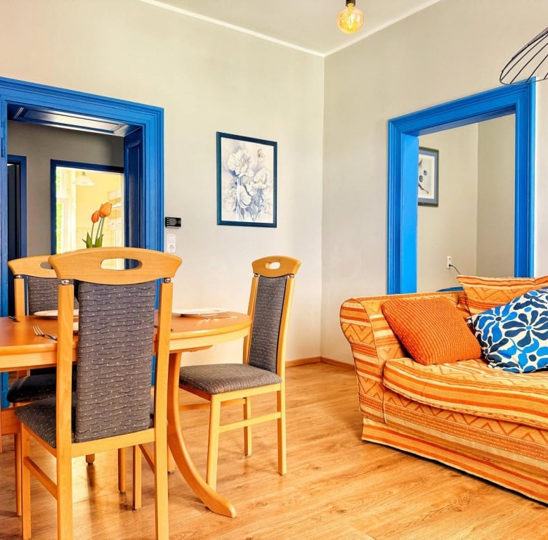 Gemütliches Wohnzimmer mit blauer Türrahmen, bequemem Sofa mit bunten Kissen und modernem Essbereich, Dekor im skandinavischen Stil, ideal für Ferienwohnungen, DEM Gruppe.